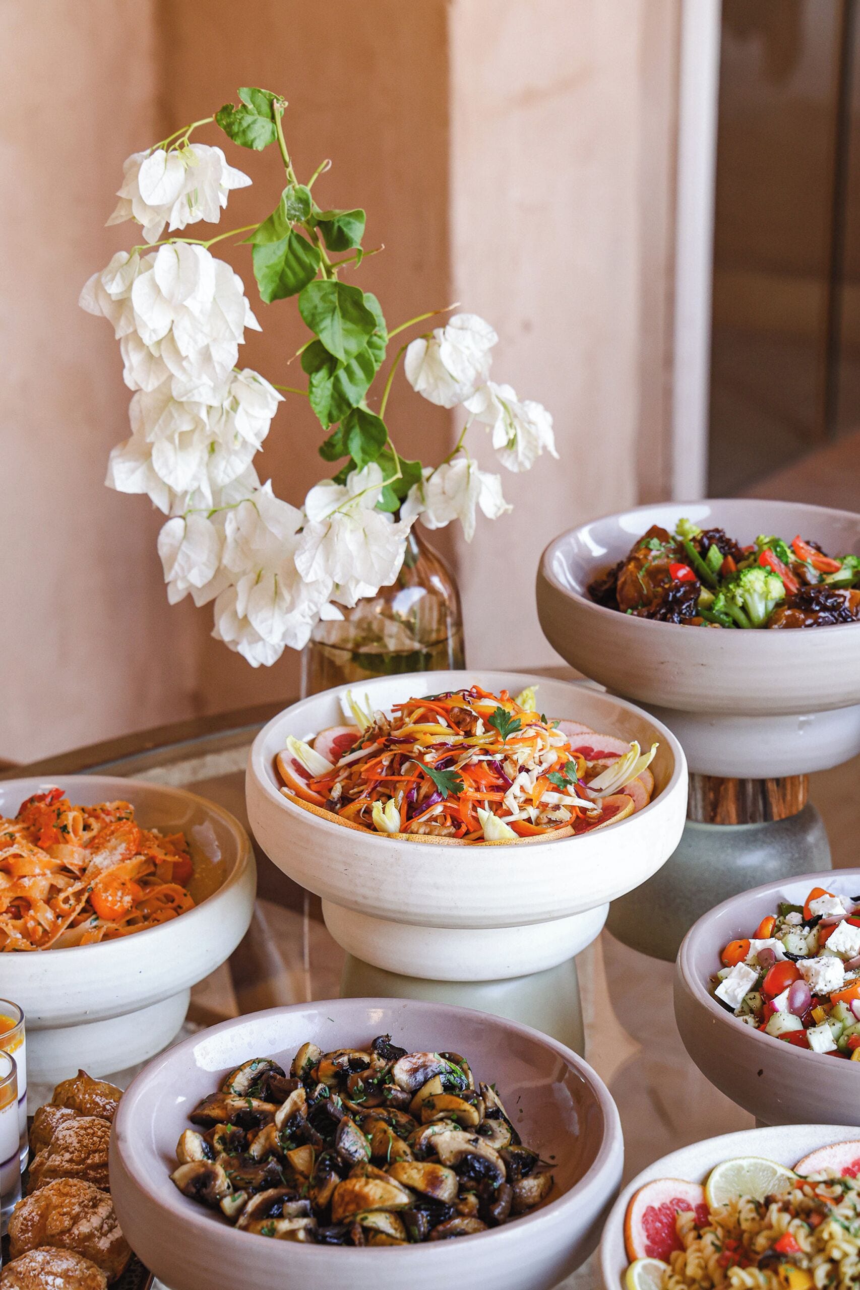 A variety of dishes in ceramic bowls, a white orchid, and a glass bottle on a table.