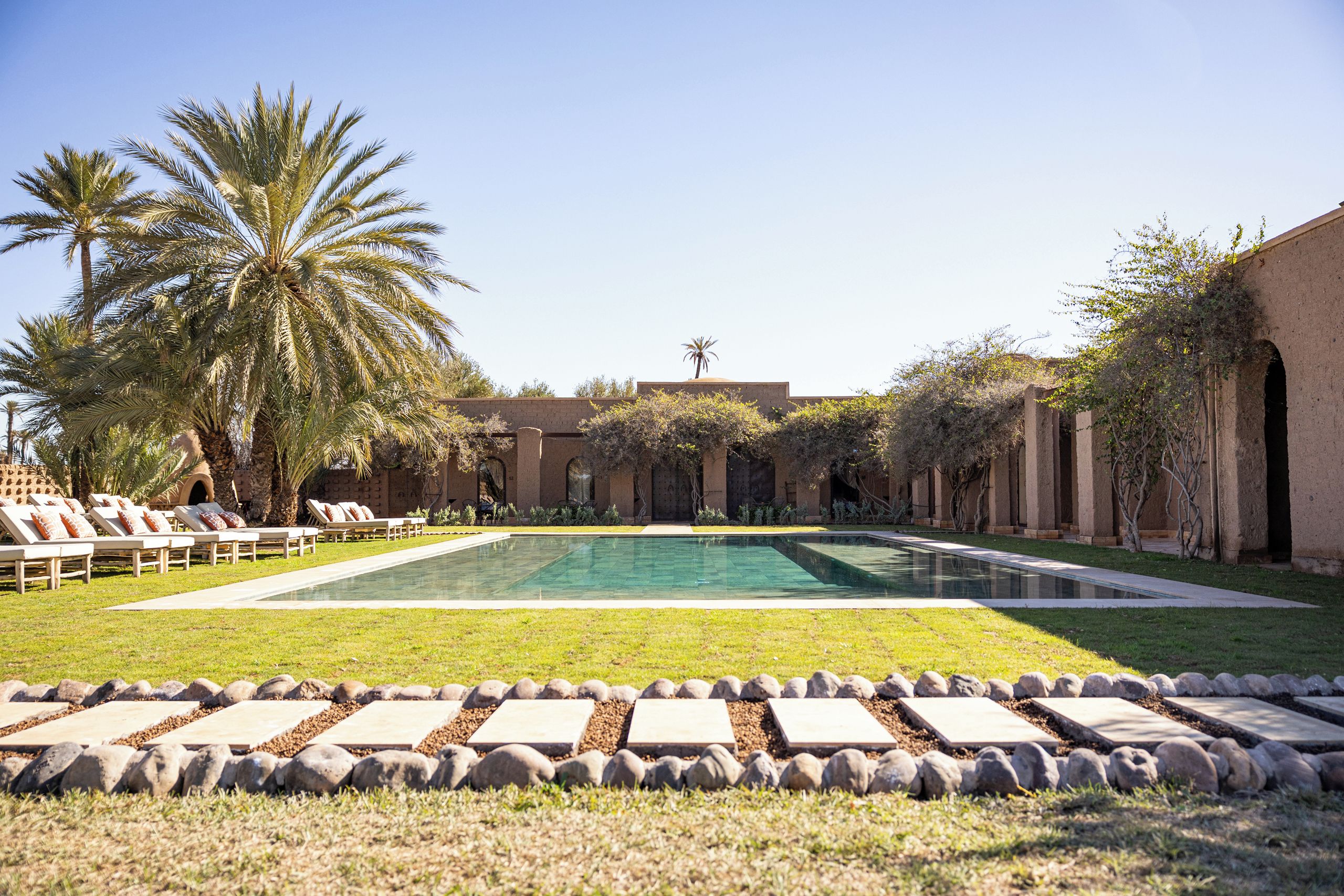 A pool area with lounge chairs, palm trees, and a clear sky.