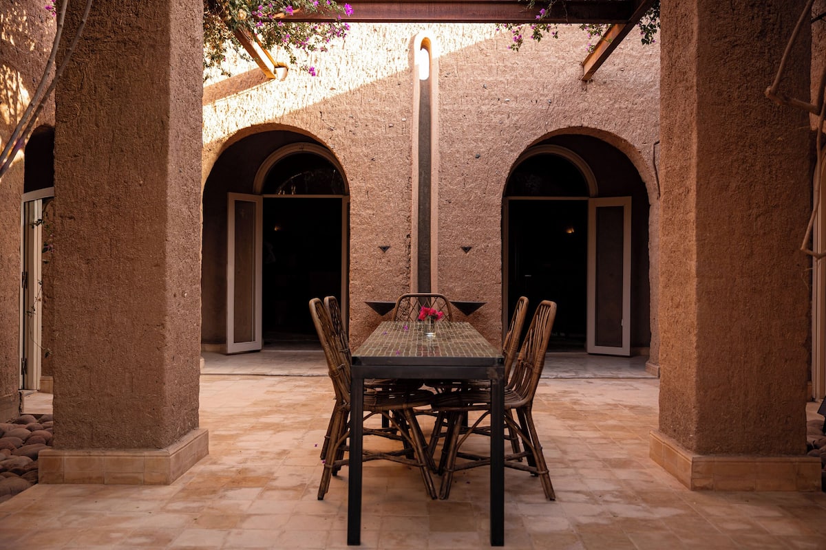 Un espacio exterior para comer con una mesa y sillas, rodeado de muros y arcos de piedra.