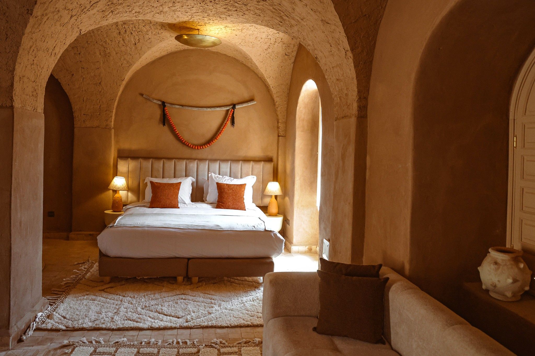 A bedroom with a large bed, two bedside lamps, a rug, and a decorative wall hanging.