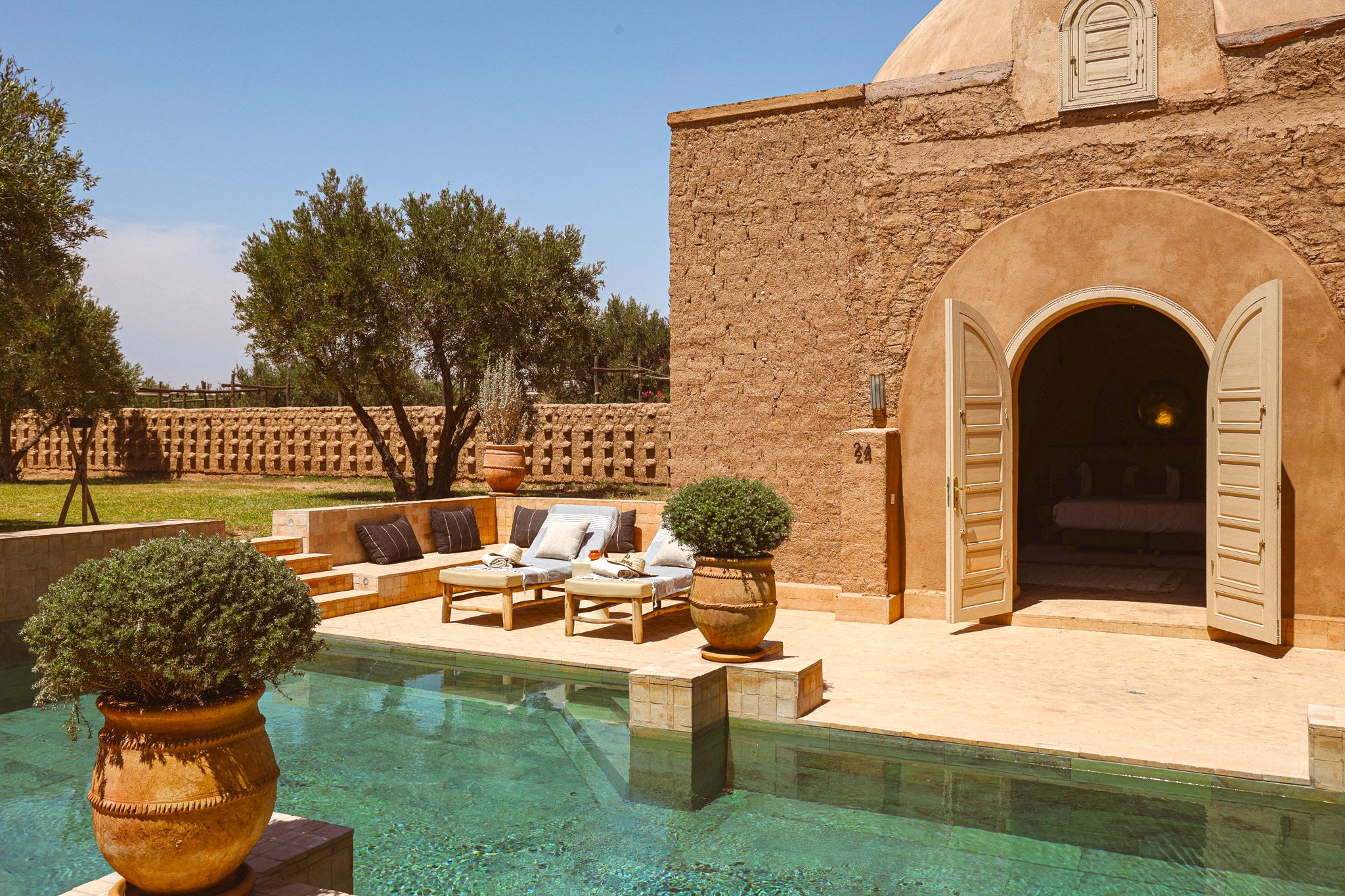 A pool area with lounge chairs and a clear pool, surrounded by a brick wall and trees.