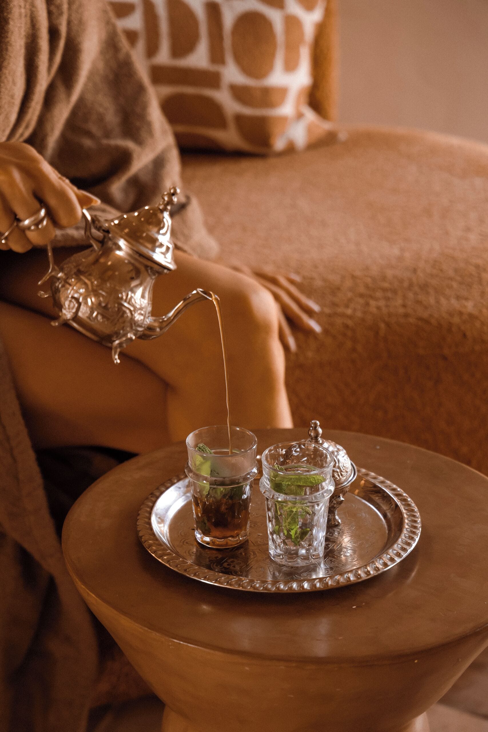 A room with a bed, a small round table with a tray holding two glasses of a beverage, and a decorative silver pitcher.