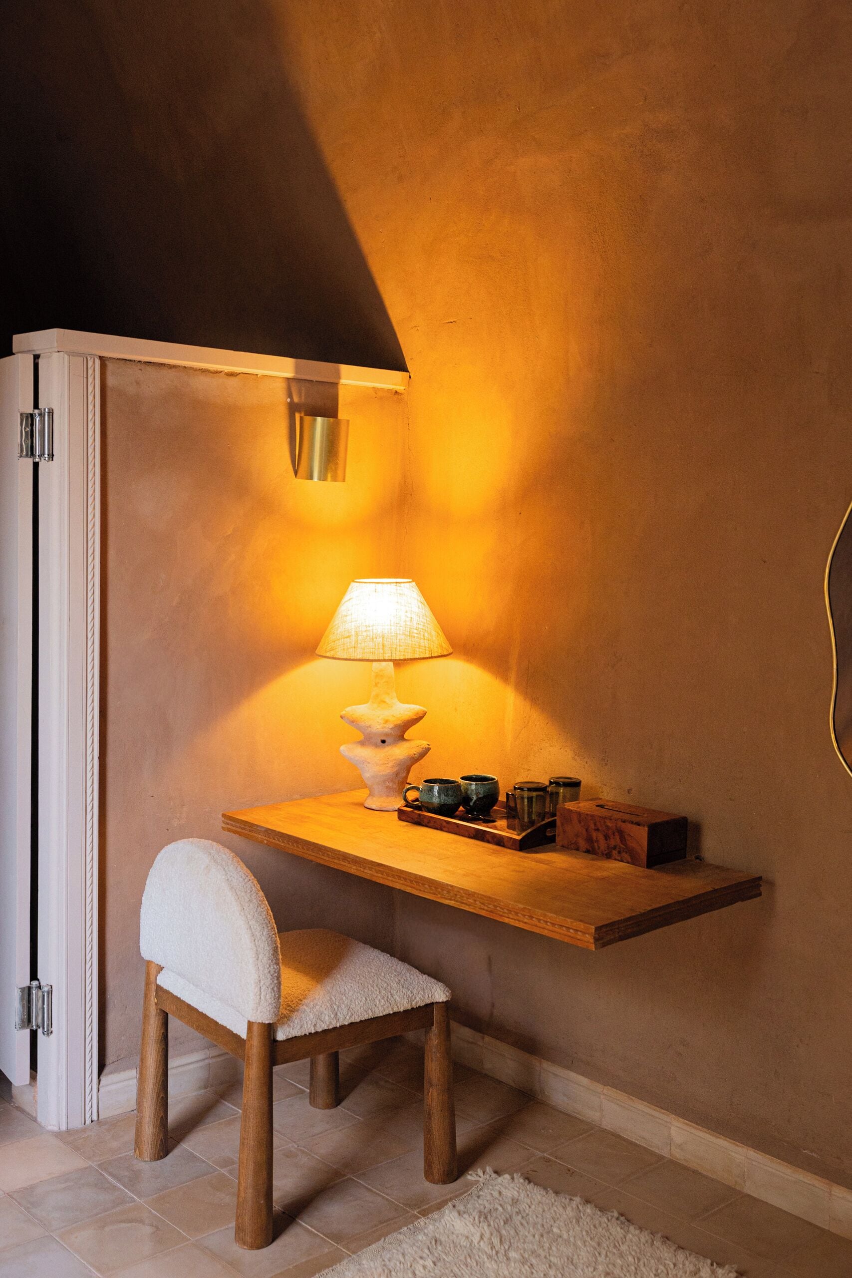 Un espacio de trabajo pequeño y acogedor con un escritorio de madera, una silla blanca y una lámpara.
