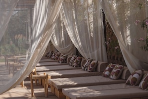 A row of beige sofas with patterned cushions, wooden tables, and a canopy of sheer white fabric. - Bliss Terra Janna (Marrakech)
