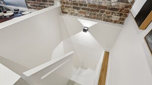 A narrow staircase with white walls and a brick accent wall. - Lavie Maison : Marais Luxury, Hoy Tub & A/C (Paris)