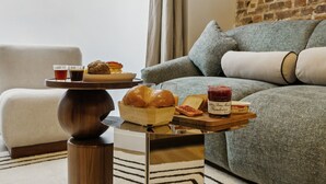A cozy living room with a grey sofa, a wooden coffee table with food items, and a brick wall in the background. - Lavie Maison : Marais Luxury, Hoy Tub & A/C (Paris)