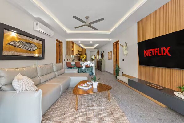 A modern living room with a sofa, coffee table, and a TV wall-mounted on the right.