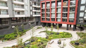 Un moderno edificio residenziale con numerosi balconi e un cortile curato con piante in vaso e un vialetto curvo.