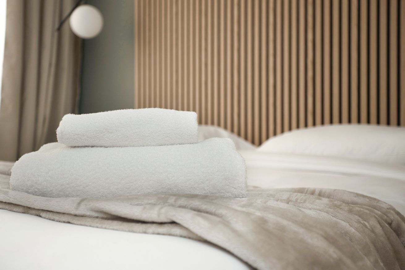 Un letto rifatto con cura, un asciugamano bianco piegato e una coperta beige.