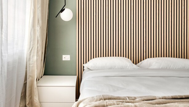 A bedroom with a bed, a bedside table, a lamp, and a wall with vertical wooden slats. - Hostmate - Milan - Imperia's Serenity - Romolo (Milan)