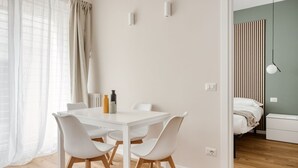 A modern, well-lit room with a white dining table, four chairs, and a bed with a striped headboard. - Hostmate - Milan - Imperia's Serenity - Romolo (Milan)