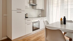 A modern kitchen with white cabinets, a built-in oven, and a dining area with a table and chairs. - Hostmate - Milan - Imperia's Serenity - Romolo (Milan)