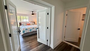Un pasillo con una cama al fondo, un ventilador de techo y una puerta que da a otra habitación.