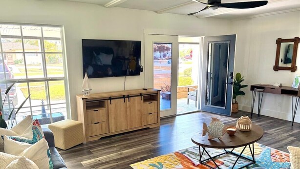 Un salón amplio con una televisión grande, armarios de madera, una mesa de centro y una alfombra colorida.