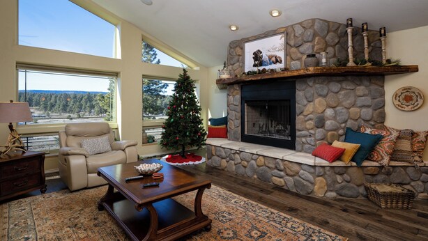 A spacious living room with a stone fireplace, a Christmas tree, and a large window overlooking a forested area. - Enjoy private luxury at Pagosa Valley Views! (Pagosa Springs)