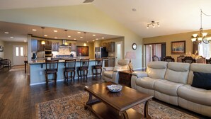 A spacious living room with a large sofa, a coffee table, and a dining area with chairs and a kitchen in the background. - Enjoy private luxury at Pagosa Valley Views! (Pagosa Springs)