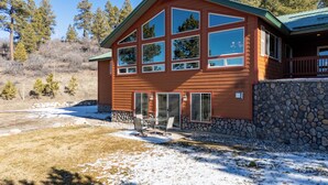 A two-story house with a stone foundation, large windows, and a patio with outdoor furniture. - Enjoy private luxury at Pagosa Valley Views! (Pagosa Springs)