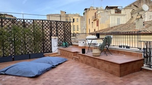 Eine Dachterrasse mit einer Matratze, einem Klappstuhl und einem kleinen Tisch.