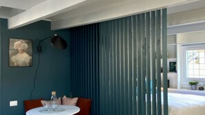 Ein Zimmer mit türkisfarbenen Wänden, einem weißen runden Tisch mit zwei Flaschen, einer braunen Couch und einem Bett mit weißer Bettwäsche.