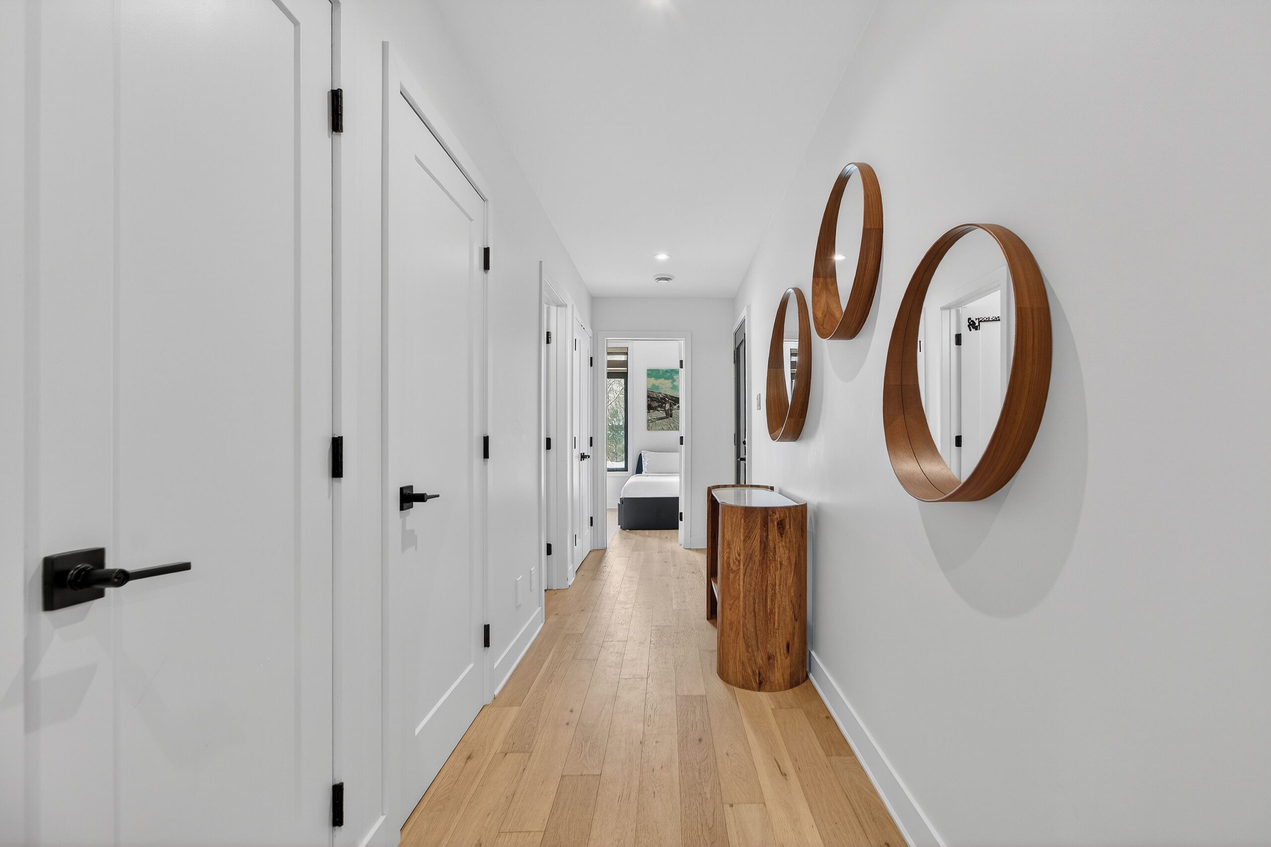 Un pasillo con puertas blancas, suelo de madera y espejos en la pared.
