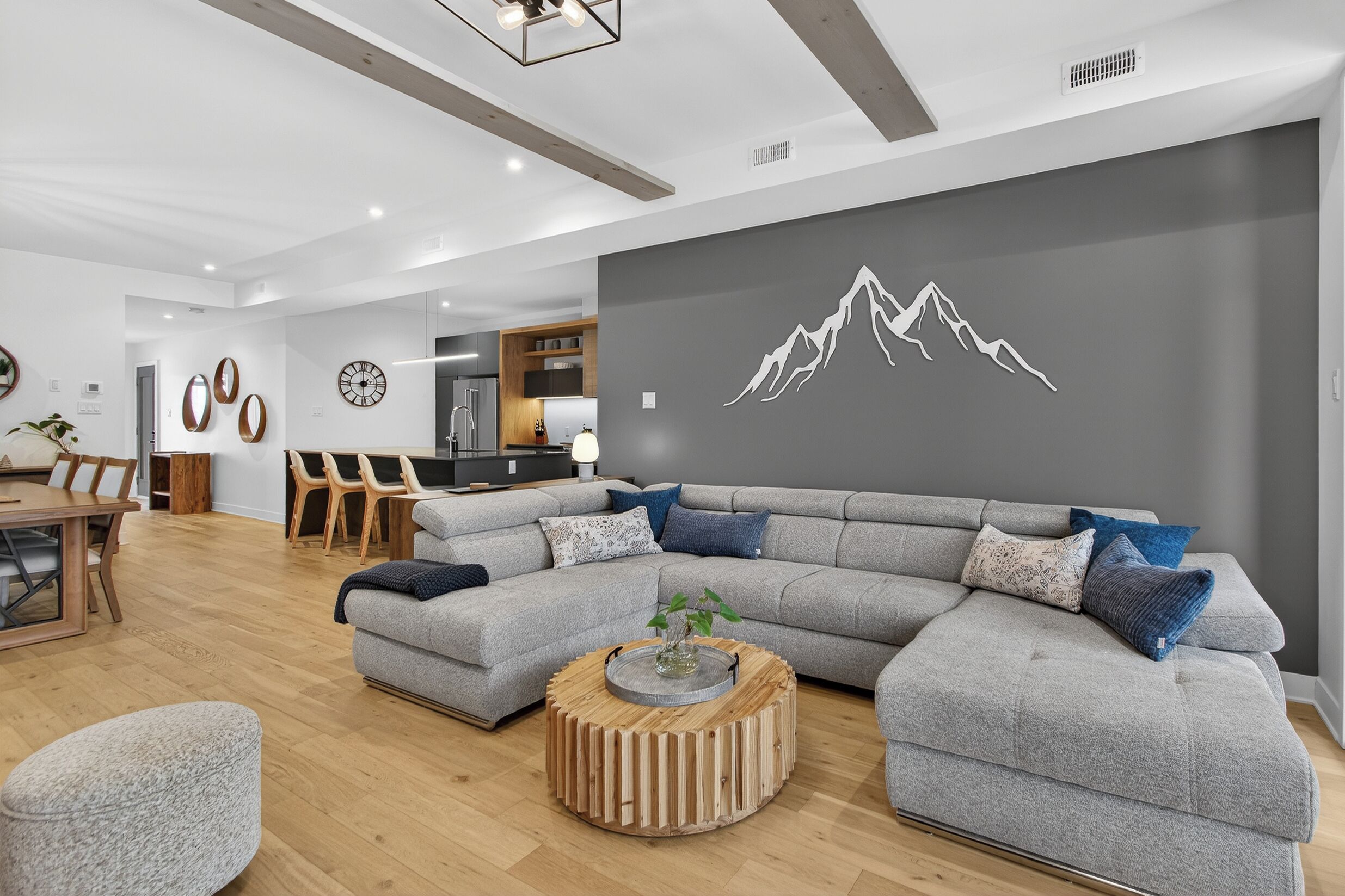 Un salon moderne avec un canapé d’angle gris, une table basse en bois et un coin repas comprenant une table et des chaises en bois.