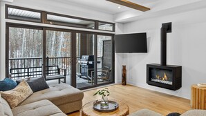 Una sala de estar moderna con chimenea, grandes puertas corredizas a una terraza y un televisor de pantalla plana montado en la pared.