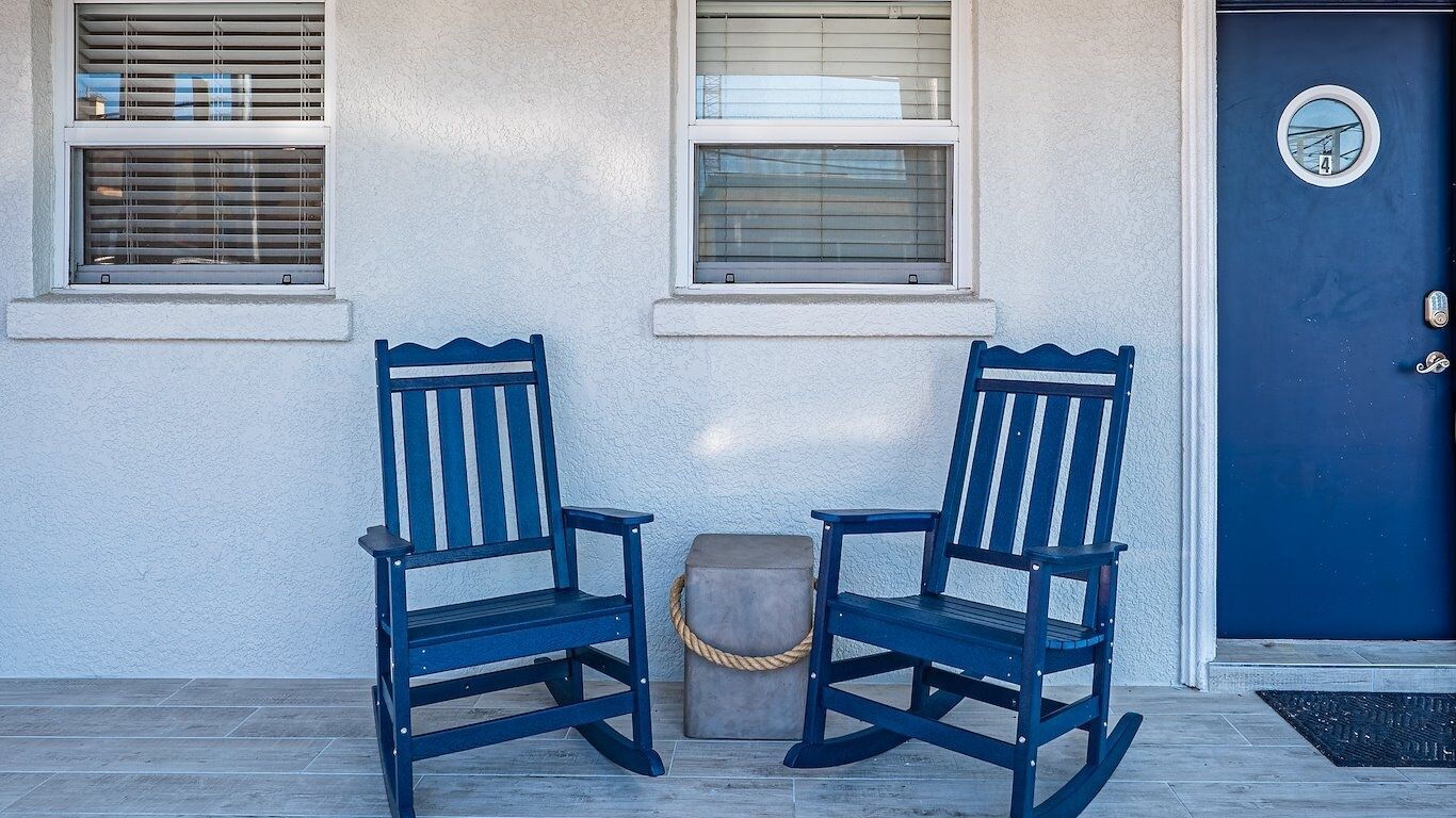 Two rocking chairs in front of a building with a blue door and two windows.