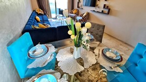 A dining area with a table set for four, blue chairs, a vase with flowers, and a sofa in the background. - Luxueux Appartement Prestigia Agate (Marrakech)