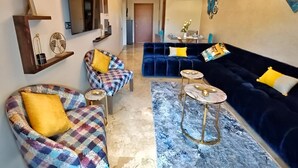 A modern living room with a blue sofa, a patterned armchair, and a round coffee table. - Luxueux Appartement Prestigia Agate (Marrakech)