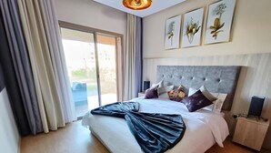 A spacious bedroom with a large bed, a sliding glass door to a balcony, and a modern headboard. - Luxueux Appartement Prestigia Agate (Marrakech)