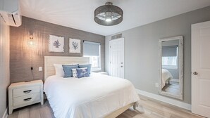 Una camera da letto con un letto, un comodino, un'opera d'arte appesa al muro e una porta con uno specchio.