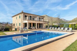 Une maison en pierre à deux étages, dotée d’une piscine, d’un espace extérieur aménagé et offrant une vue sur les montagnes.