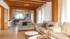 Amplia sala de estar con un sofá seccional beige, una mesa de centro redonda y vigas de madera en el techo.