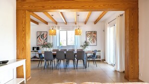 Un comedor espacioso con techo de madera, una mesa larga con sillas y luces colgantes.