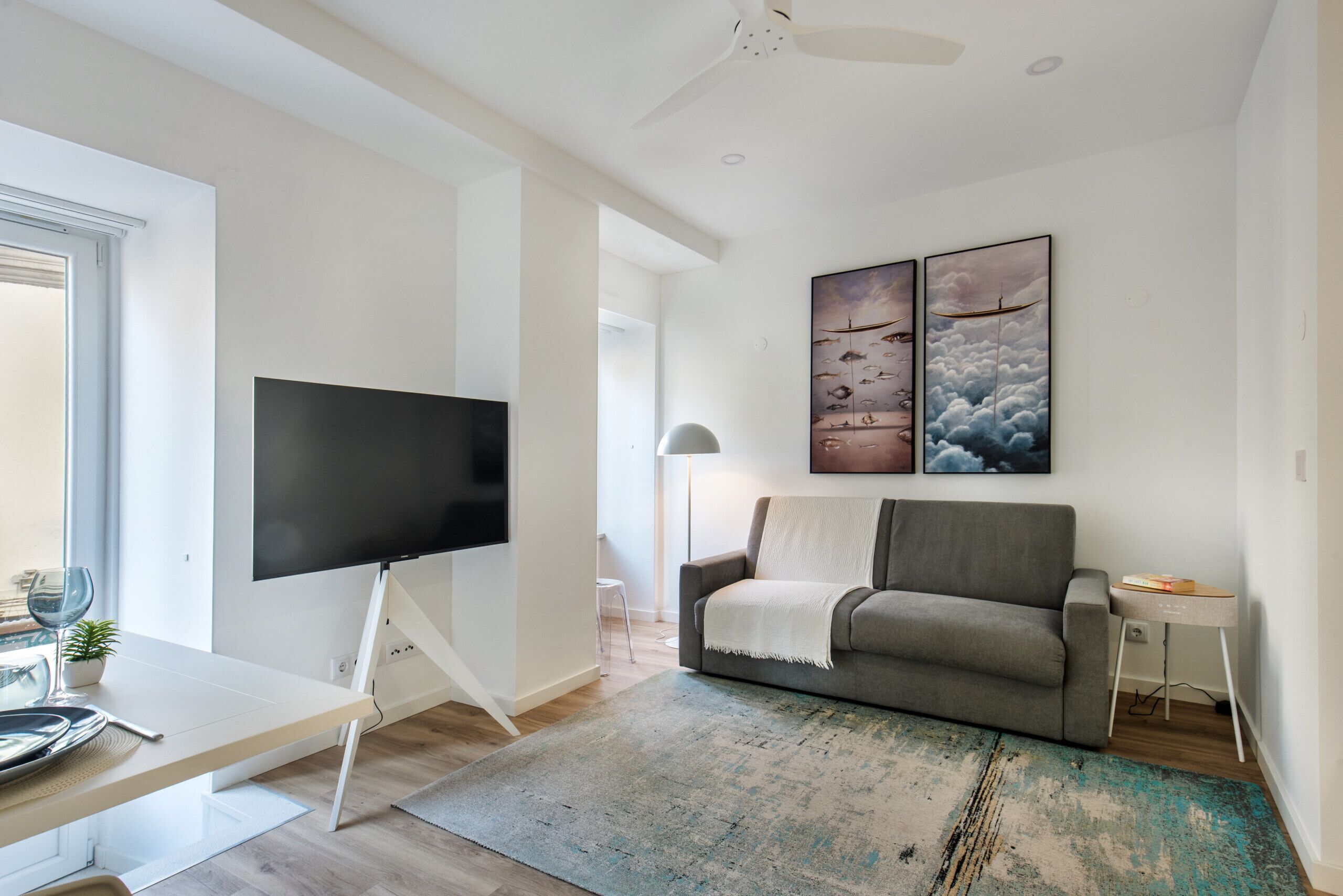 A modern living room with a flat-screen TV, a grey sofa, and two framed artworks on the wall.