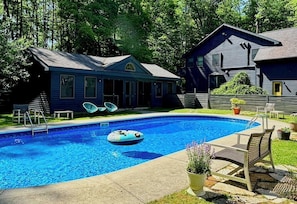 Piscina com um boi flutuante, rodeada por um deck com cadeiras e um pequeno edifício.