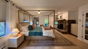 Une chambre à coucher avec un lit, des tables de chevet, un tapis, une cheminée et une vue sur l’extérieur.