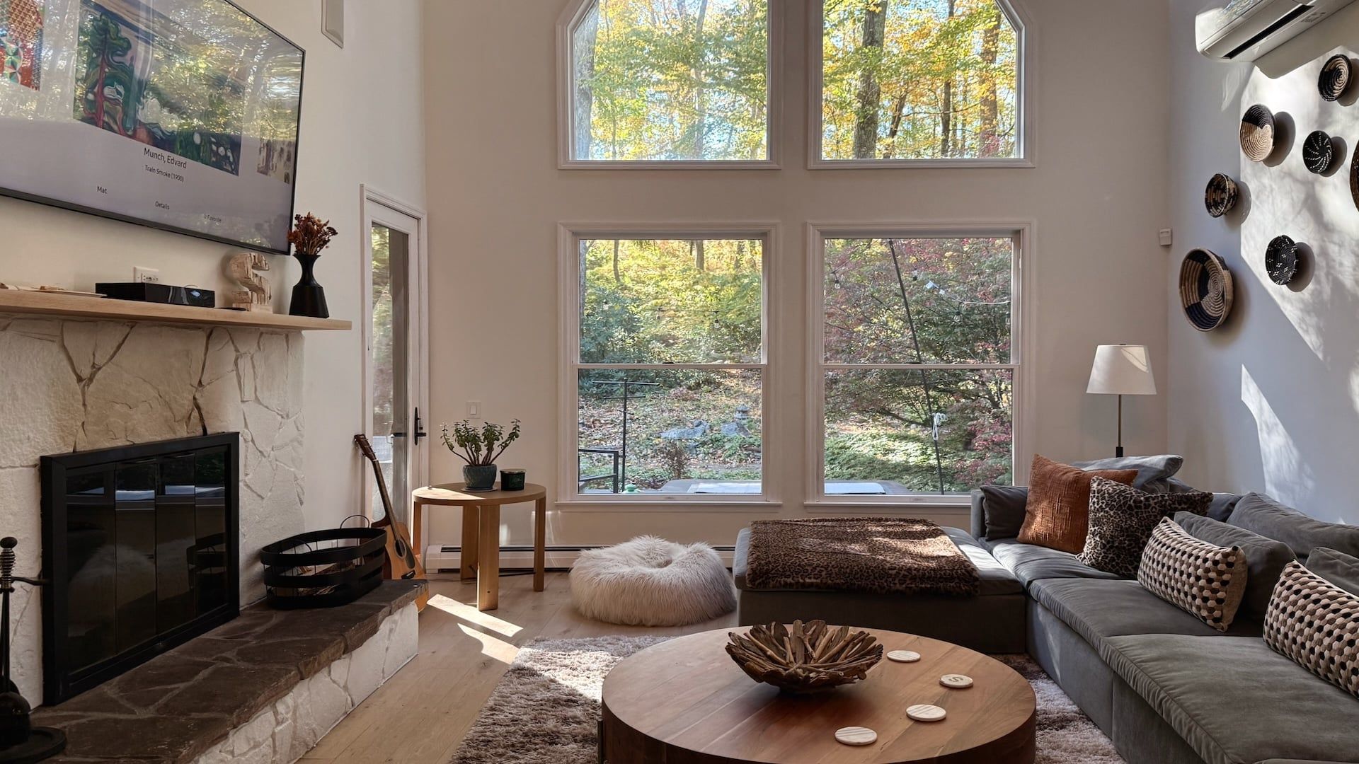 A living room with a fireplace, a sofa, a coffee table, and large windows with a view of trees.