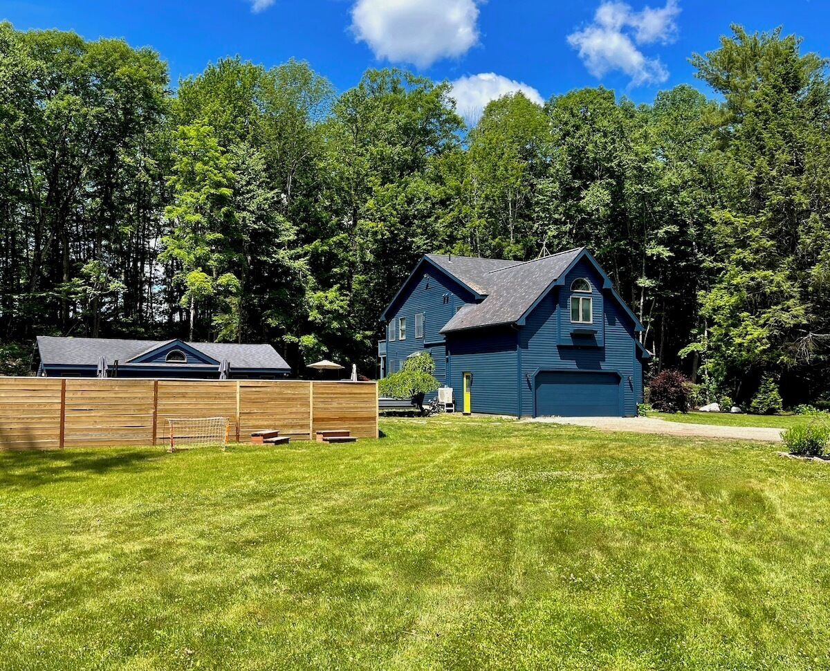 A blue house with a dark roof, surrounded by a wooden fence and a well-maintained lawn.