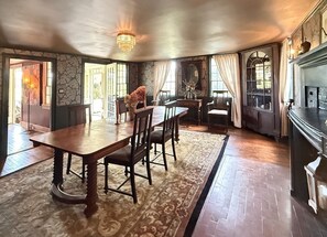 A dining area with a wooden table and chairs, a patterned rug, and a fireplace.