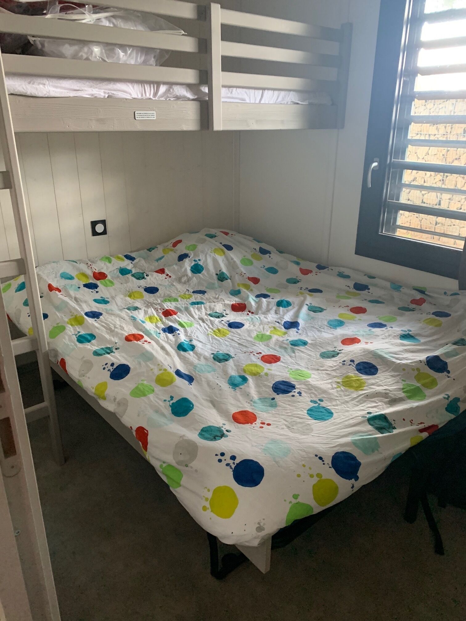 A bunk bed room with a polka dot bedspread, a window with a view, and a door.