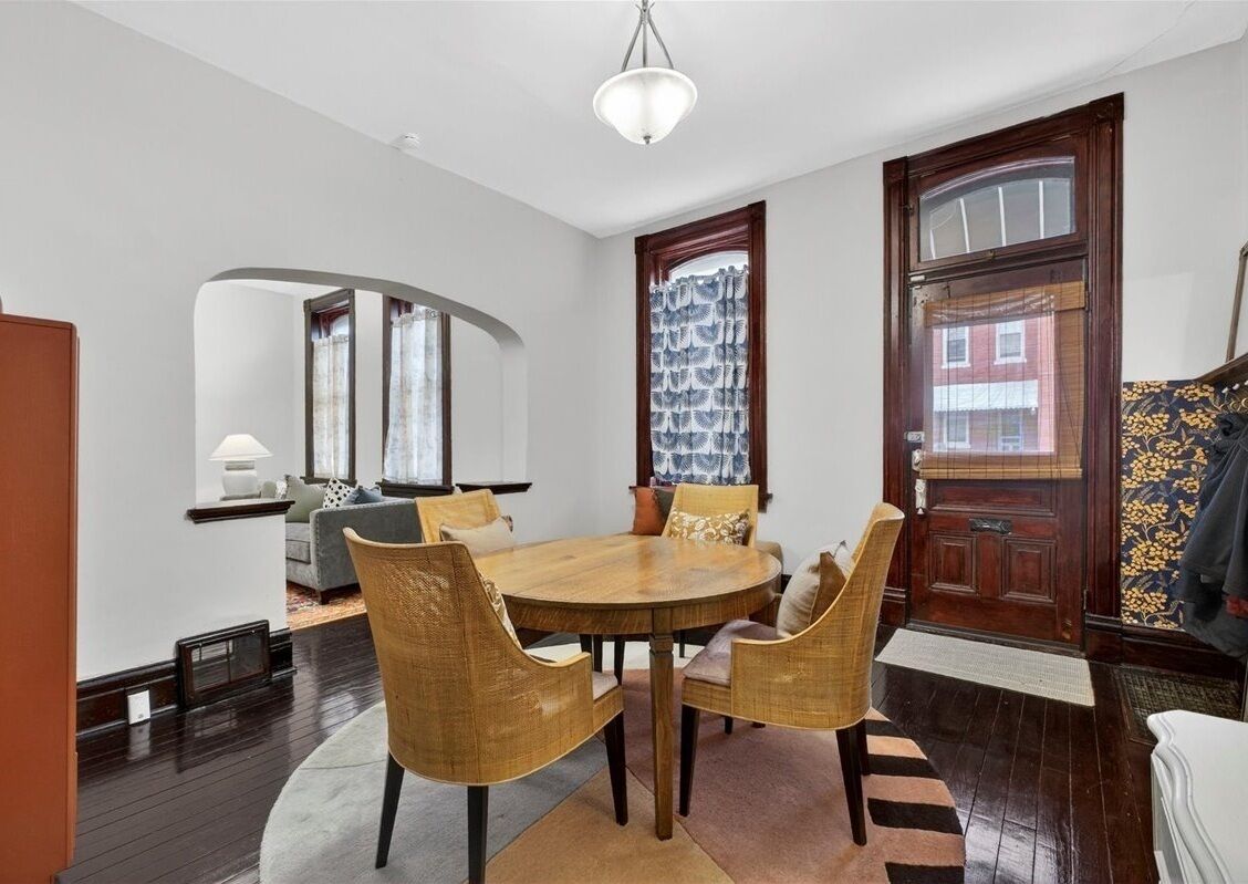 A dining area with a round wooden table, wicker chairs, and a chandelier.