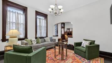 A living room with a sofa, two armchairs, a patterned rug, a lamp, and a chandelier.