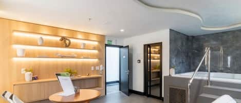 A modern hotel lobby with a reception desk, lounge chairs, a reception area with a wooden wall and shelves, and a spa area with a bathtub and shower.