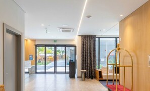 A hotel lobby with a reception desk, a seating area with a sofa and armchairs, a large window with a view of the outdoors, and a red carpet leading to the entrance. - Apt 300m From the Beach in Bldg w/ Pool Fnk1905 (Itapema)
