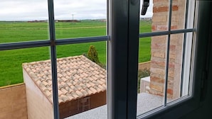 A view from a window with a tiled roof and brick wall, overlooking a green field.