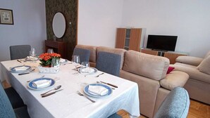 A dining area with a table set for four, a sofa, and a TV.