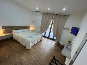 A hotel room with a bed, bedside table, lamp, air conditioning unit, curtains, and a TV mounted on the wall. - In the center of Naples, 200m Central Station (for Pompeii, Amalfi, Sorrento...) (Napoli)