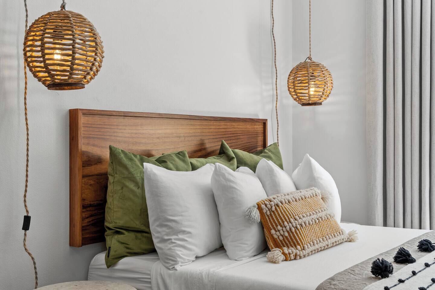 Un lit bien fait, avec une tête de lit en bois, plusieurs oreillers et une couverture en tissu tissé.