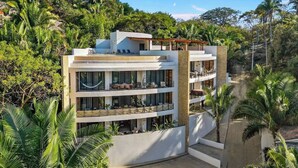Un hotel de varios pisos con balcones, rodeado de exuberante vegetación.